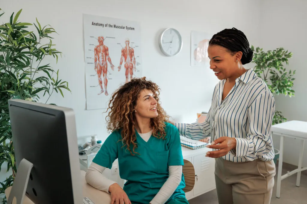 Two healthcare professionals talking by computer